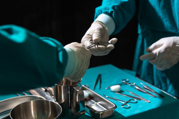 Two surgeons working in operating room, one hand over surgical equipment to another. Surgeons hands holding surgical scissors and passing surgical equipment,