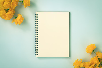 Spiral Notebook or Spring Notebook in Unlined Type and Orange Flowers at Bottom Right and Top Left Corner on Blue Pastel Minimalist Background. Spiral Notebook Mockup on Center Frame in Vintage Tone