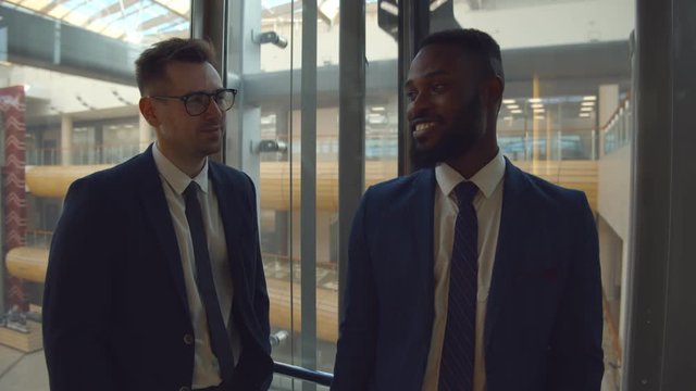 Young diverse colleagues smiling and chatting lifting in glass elevator