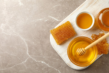 Composition with honeycombs, honey, jars and dipper on gray table