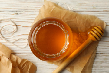 Glass jar of honey and dipper on white wooden table, top view