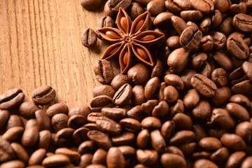 Anise and a lot of coffee beans lie on a wooden table. There is an empty space at the top right.