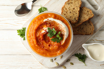 Composition with bowl of pumpkin soup on white wooden background, top view