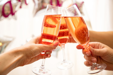 Three girlfriends having party and drinking shampagne. Glasses with pink champagne in the hands of women