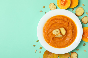 Composition with plate of pumpkin soup on mint background