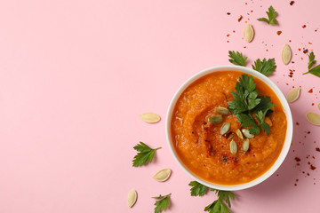 Composition with bowl of pumpkin soup on pink background, top view