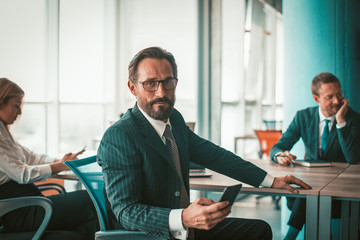 Naklejka na ściany i meble Confident businessman and creative team working in office. Male project manager looks at camera against background of colleagues seated at negotiation table. Tinted image.