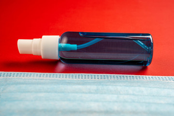 Close-up view of disinfectant and face mask. Cropped disposable mask with hand sanitizer on red background.