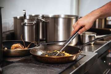Chef cooking black pasta in a pan with tongs