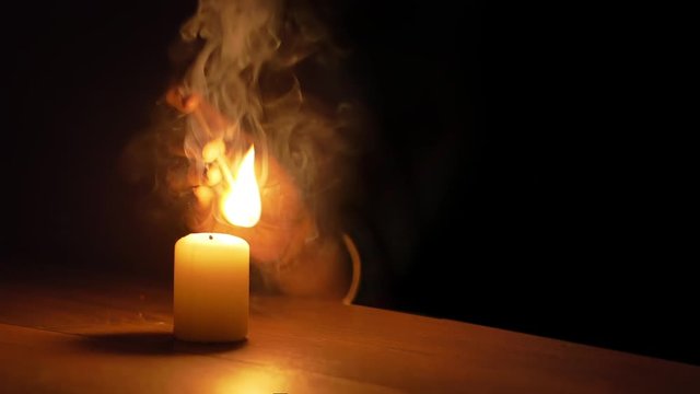 Female hand lighting a candle with a large flame of a long match, low-key slow motion with black background  
