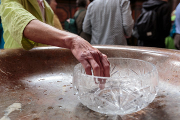 An older religious person dips their hand in a holy water glass container when leaving the church, after mass.