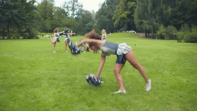 Beautiful Cheerleader doing cartwheel on grass with teammates practicing on background