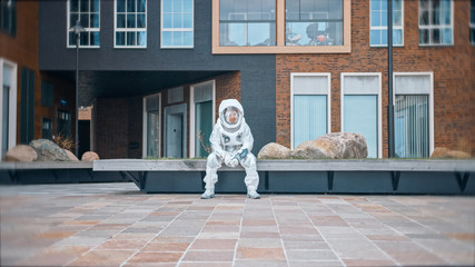 Fototapeta na wymiar Sad Man in Spacesuit is Sitting on Wooden Bench. Miserable Astronaut Looks Down. Emotionally Depressed Spaceman in White Futuristic Suit with Technological Panel on His Hand.