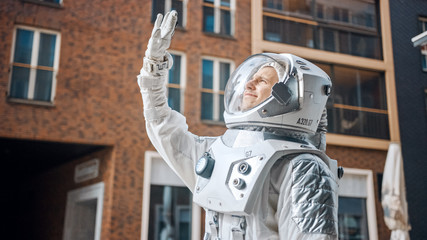 Fototapeta na wymiar Low Angle Footage of a Confident Handsome Astronaut Looking at the Bright Blue Sky and Covers the Sun with His Hand. Man in Futuristic Suit with Technological Panel on His Hand. Modern Neighbourhood.
