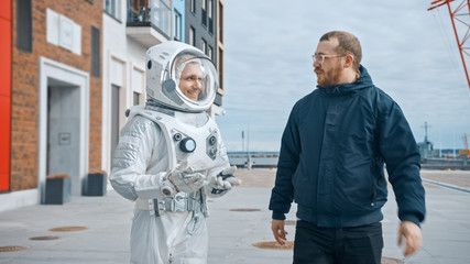 Ironic and Satirical Shot of Man in Spacesuit Walking on a Street with a Friend in Casual Clothes....