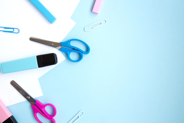 White sheets of paper, colorful markers, erasers, clips and scissors on blue background with space for text. School stationery and supplies. Colorful set of stationery for girls. Back to school
