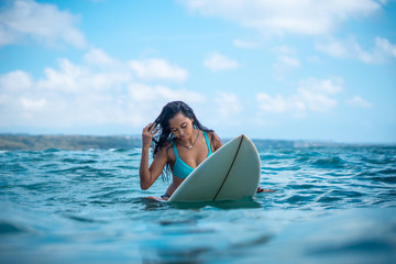 Portrait of surfer girl on white surf board in blue ocean pictured from the water