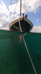 Underwater split photo of traditional classic wooden fishing boat anchored in tropical exotic...