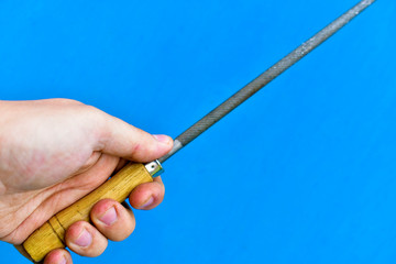 Fototapeta premium Iron round file with wooden handle in hand on blue background