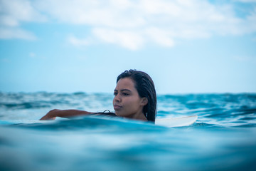 Portrait of surfer girl on white surf board in blue ocean pictured from the water in Bali