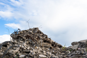 Concrete fragments of the remains of a destroyed building against a blue sky with gray clouds....