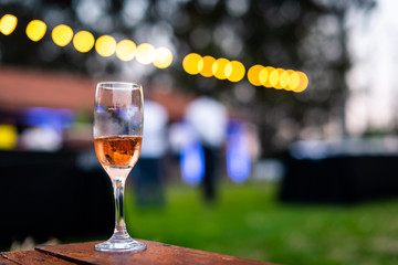 one glass of champagne in focus with outdoors party out of focus in background