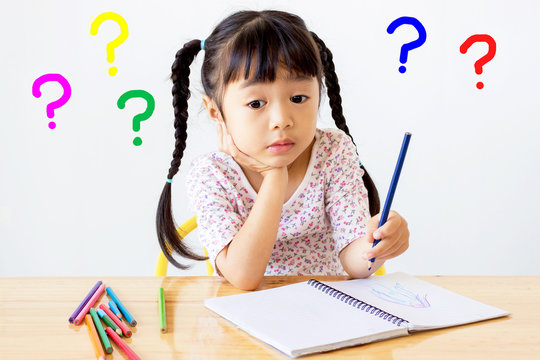 asian child has a problem of left hand , is drawing by pencil colors on a notebook rest her chin on her hand with colorful question mark signs on white background
