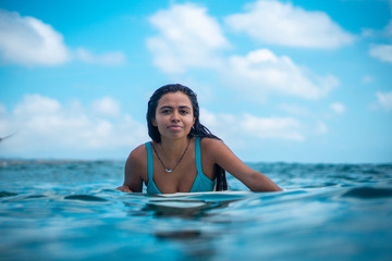 Portrait of surfer girl on white surf board in blue ocean pictured from the water