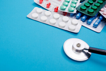 Pills in blister with stethoscope on blue background. Flat lay, copy space, top view. Health concept.