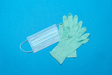 Disposable blue medical face mask and rubber latex gloves on blue background