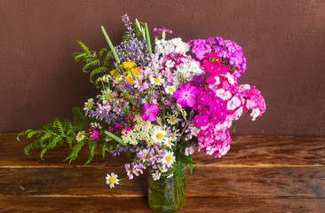 Bouquet of field flowers in glass vase on brown table