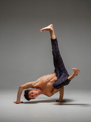 Cool man dancer with naked torso dancing lower break dance isolated on gray background