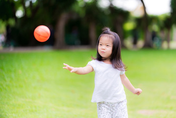 Excited little cute girl playing orange ball on soccer field outdoors. Adorable kid throwing small...