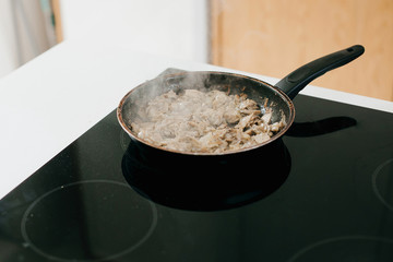 Roasted mushrooms and onion on electric stove on modern white kitchen. Process of making home pizza, ingredients close up. Home cooking concept.