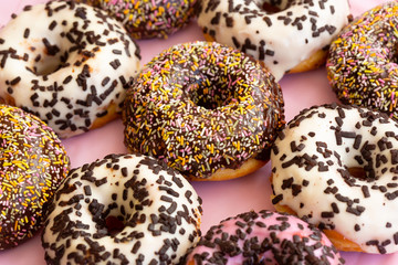 Close up view of delicious colourful donuts with sprinkles and chocolate flakes . Assorted donuts with chocolate frosted, white and pink glaze and sprinkles. Selective focus.