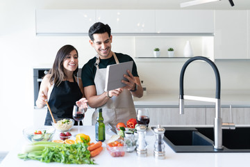 Obraz na płótnie Canvas Young Couple Preparing Food Through Online Recipe