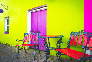 Colorful terrace set up with retro style chairs; table and green wall, purple entrance doors