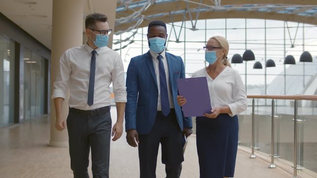 Business team wearing protective masks walking in modern office corridor