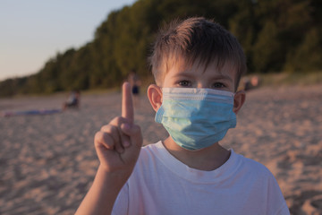 Little boy in a medical mask on the beach. Life after the coronavirus pandemic, travel and vacation...