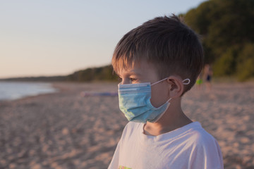 Little boy in a medical mask on the beach. Life after the coronavirus pandemic, travel and vacation...