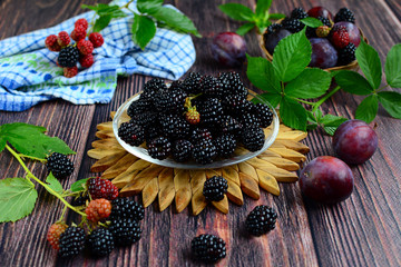Fresh berries and leaves of blackberries and purple ripe plums on a brown wooden background.