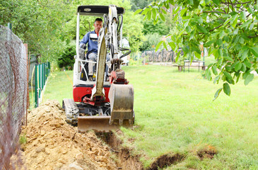 Workman using a mini digger to excavate a hole in the garden. Czech republic, Europe.