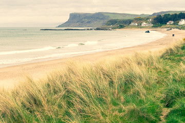Fototapeta na wymiar Wild Ballycastle beach with tourists walking and fair head cliff in the background