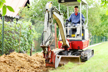Workman using a mini digger to excavate a hole in the garden. Czech republic, Europe.