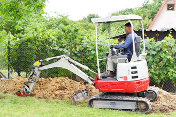Workman using a mini digger to excavate a hole in the garden. Czech republic, Europe.