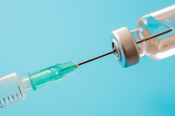 Vaccine vial dose and syringe against pale blue background