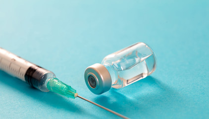 Vaccine vial dose and syringe against pale blue background