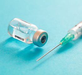 Vaccine vial dose and syringe against pale blue background