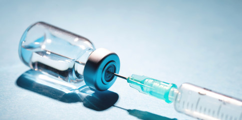 Vaccine vial dose and syringe against blue background