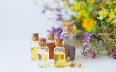 Essential oils in glass bottles with organic healing herbs and flowers in the light background